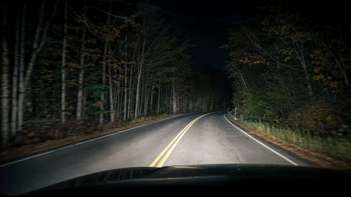 Unlit country road in Quebec at night, with car headlights illuminating the forest and pavement ahead